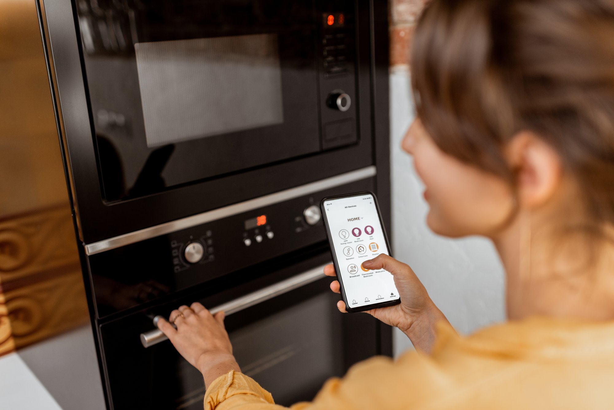 Woman controlling kitchen appliance through app on her phone Woman controlling kitchen appliance through app on her phone